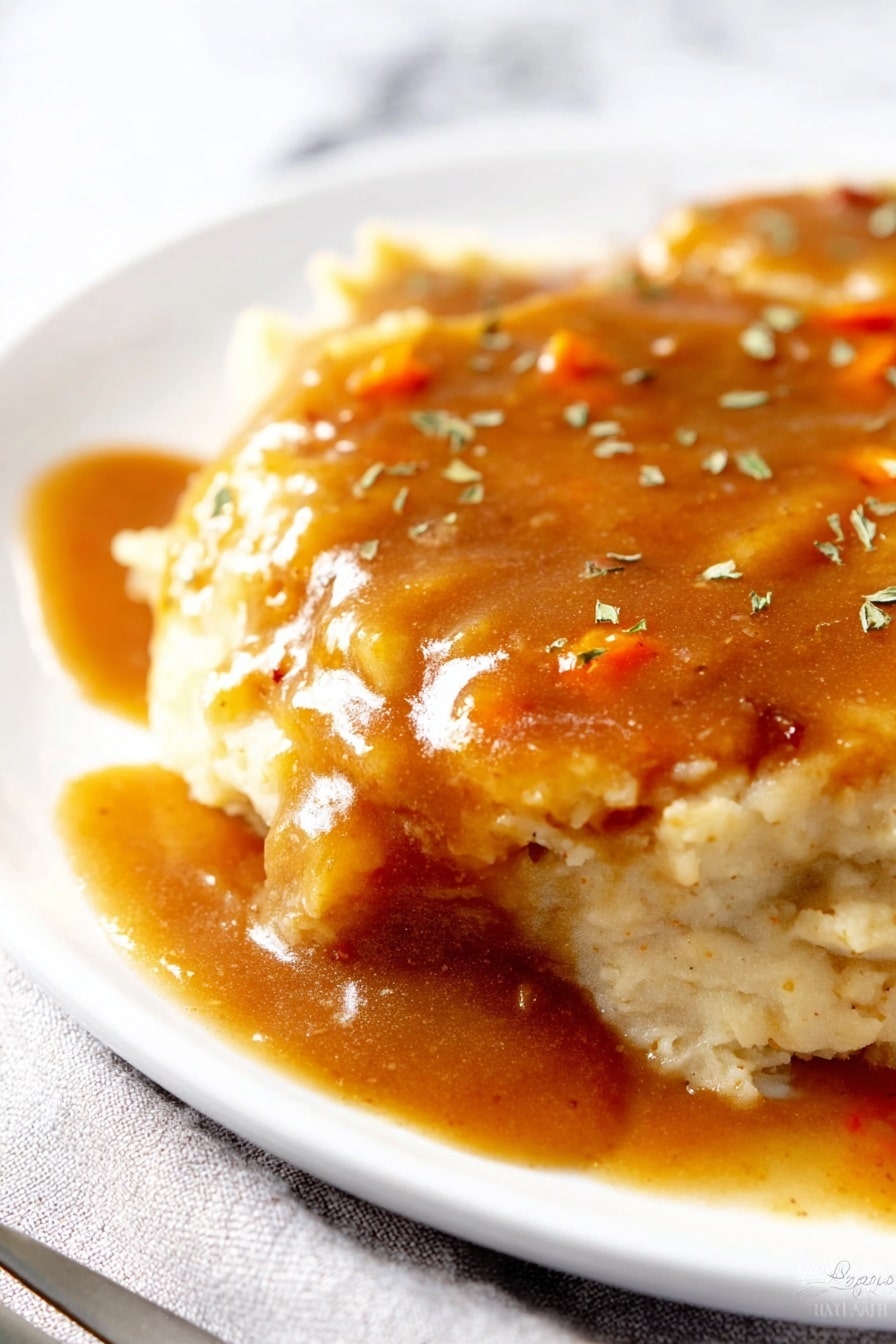 A close-up of a plate with two layers of light beige mashed potatoes, soft and creamy in texture. On top, there is a thick layer of brown gravy with a shiny, smooth texture, containing small orange bits, possibly carrots. The gravy is spread evenly, slightly dripping on the sides. The dish is sprinkled with small green herb pieces. The white plate rests on a white marbled surface with a silver fork partially visible on the bottom left side. Photo taken with an iphone --ar 2:3 --v 7 - Creamy Cabbage and Carrot Coleslaw, healthy coleslaw recipes, easy vegetable salads, vegan-friendly coleslaw, refreshing summer salads
