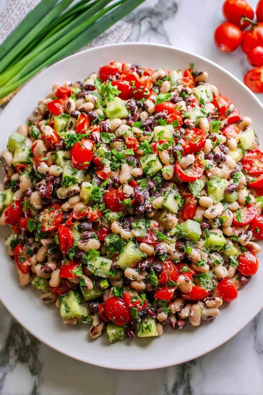 A large white plate holds a mixed bean salad piled high with many colorful ingredients. The salad has three main layers visible: the base layer is made of small, round white and black beans mixed closely together, the middle layer is scattered chopped bright red cherry tomatoes and green cucumber pieces, and the top layer is sprinkled with chopped fresh green herbs that add a fresh, leafy texture. The salad looks fresh and slightly glossy, suggesting a light dressing. The plate sits on a white marbled surface, with green onions and red cherry tomatoes placed nearby for decoration. photo taken with an iphone --ar 2:3 --v 7 - Mediterranean Bean Salad with Feta, healthy bean salad, easy Mediterranean salad, vegetarian bean salad, quick summer salad