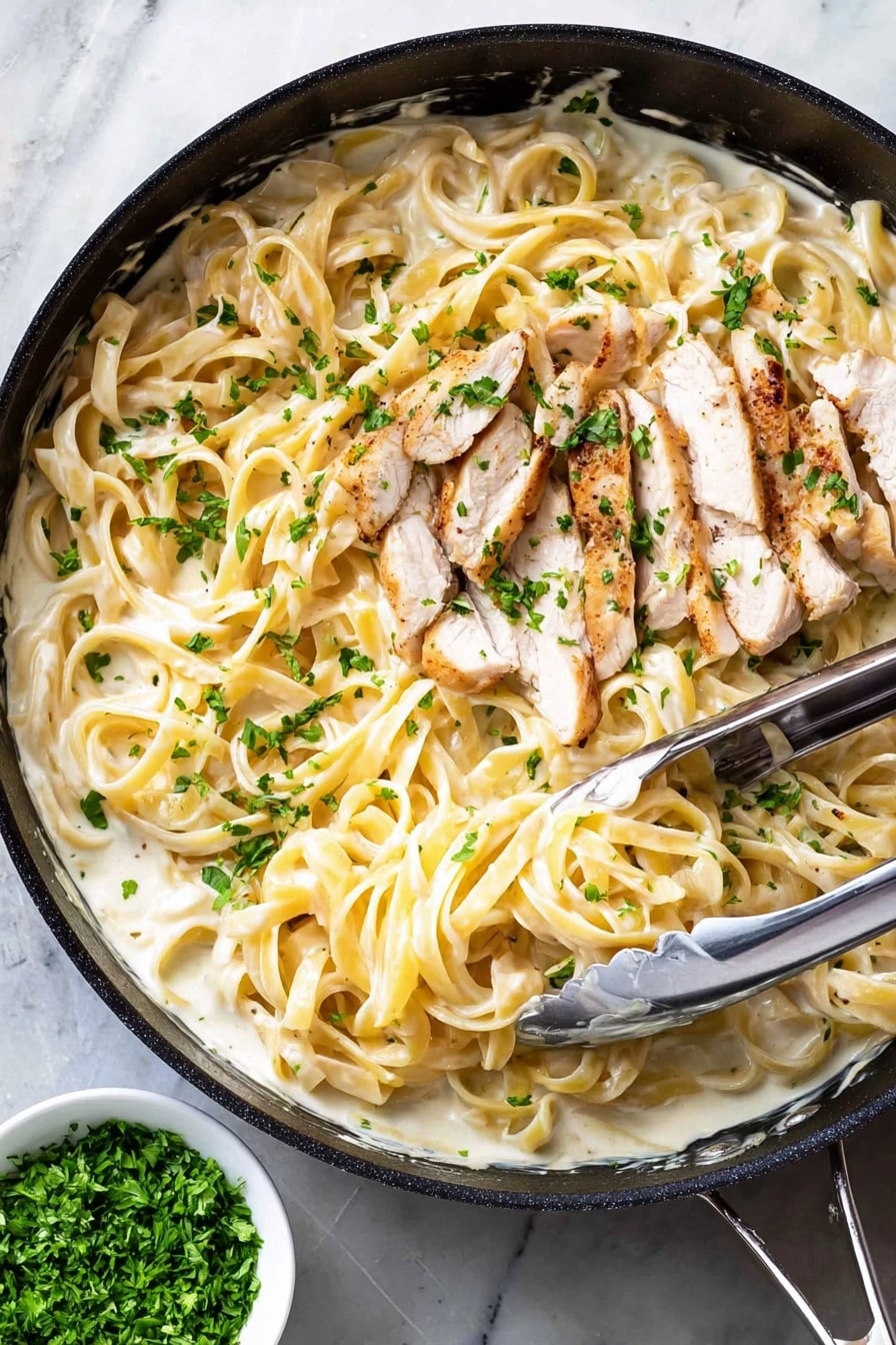 The image shows a black pan filled with creamy white sauce mixed with long, light yellow fettuccine noodles. On top of the noodles, there are several thin slices of cooked white meat with light brown edges. Small green parsley pieces are sprinkled all over the dish, adding a fresh touch. A pair of metal tongs rests inside the pan, slightly lifting some of the noodles. The pan is placed on a white marbled surface, and next to it is a small white bowl containing finely chopped green herbs. Photo taken with an iphone --ar 2:3 --v 7 - One Pot Chicken Alfredo Pasta, One Pot Alfredo, Easy Chicken Alfredo, Creamy Chicken Pasta, Quick Alfredo Dinner