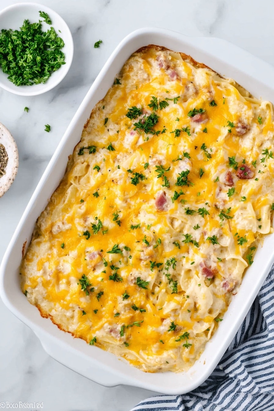 In the image, there is a white rectangular baking dish filled with creamy pasta that has a thick layer of melted yellow cheese on top. The pasta is visible under the cheese, showing a mix of white noodles and small pieces of light brown and pinkish ingredients, likely meat. Fresh green herbs are sprinkled over the cheese, adding a touch of color. The dish sits on a white marbled surface, with a small white bowl of chopped green herbs placed to the side and a blue and white striped cloth nearby. The top of the pasta has a slightly shiny texture from the cheese. Photo taken with an iphone --ar 2:3 --v 7 - Cheesy Chicken Spaghetti Bake, easy cheesy chicken casserole, comforting pasta bake, creamy chicken spaghetti, family-friendly pasta dish