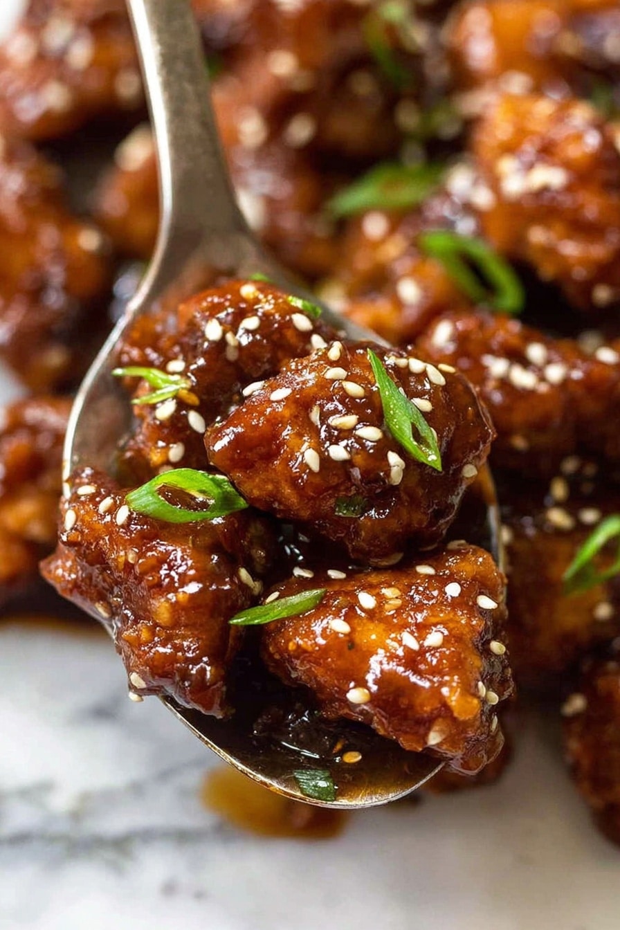 The image shows a close-up view of small pieces of fried chicken coated in a thick, shiny, dark brown sauce. The chicken pieces are irregular in shape with a crispy texture underneath the sauce. White sesame seeds are scattered on top, adding contrast and texture. Thin green slices of scallions or green onions are sprinkled over the chicken, providing a splash of fresh color. The chicken rests in a metal spoon, with more saucy chicken pieces visible in the background, all set on a white marbled surface. photo taken with an iphone --ar 2:3 --v 7 - Crispy General Tso's Chicken, Chinese chicken recipes, homemade takeout chicken, spicy sweet chicken stir-fry, easy Asian chicken dish
