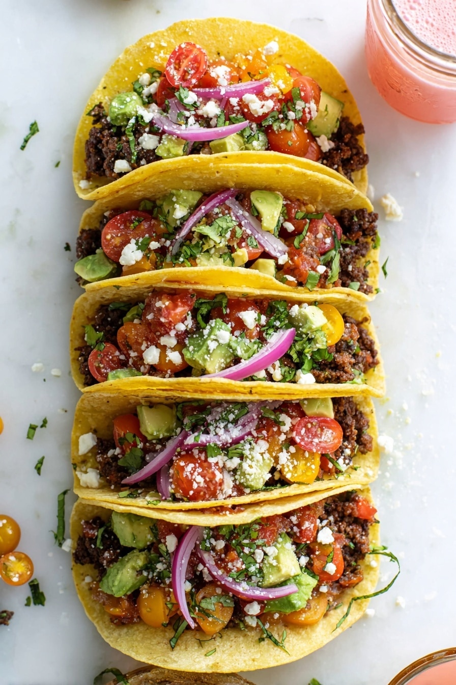 Four soft yellow corn tacos are stacked vertically over a white marbled surface. Each taco has a base layer of crumbled dark brown seasoned ground meat, topped with a colorful salad mix of chopped red and yellow cherry tomatoes, green avocado chunks, and fresh green cilantro. Thin slices of bright purple-red onions curve on top, with some white crumbly cheese sprinkled in between the layers. To the upper right, a small glass jar with a pink drink is partially visible. The scene is bright and fresh, showing vibrant colors and textures. photo taken with an iphone --ar 2:3 --v 7 - Easy Ground Beef Tacos, ground beef tacos, quick taco recipes, homemade beef tacos, weeknight taco dinner