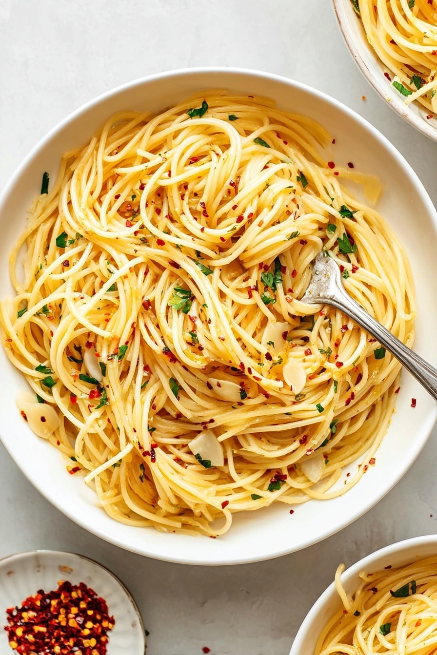 A large white bowl filled with long, thin spaghetti noodles that are lightly coated with olive oil, giving them a soft yellow color. Scattered throughout the pasta are thin, flat slices of garlic and small bits of fresh green parsley. Tiny red chili flakes are sprinkled evenly on top, adding small pops of red. A silver fork is twirling a small bundle of the pasta near the center of the bowl. The bowl rests on a white marbled surface, with a small white plate next to it containing additional red chili flakes. Part of another similar bowl filled with the same pasta can be seen in the upper right corner. Photo taken with an iphone --ar 2:3 --v 7 - Garlic Spaghetti Aglio e Olio, easy garlic pasta recipe, quick spaghetti dinner, simple Italian pasta dish, flavorful garlic pasta
