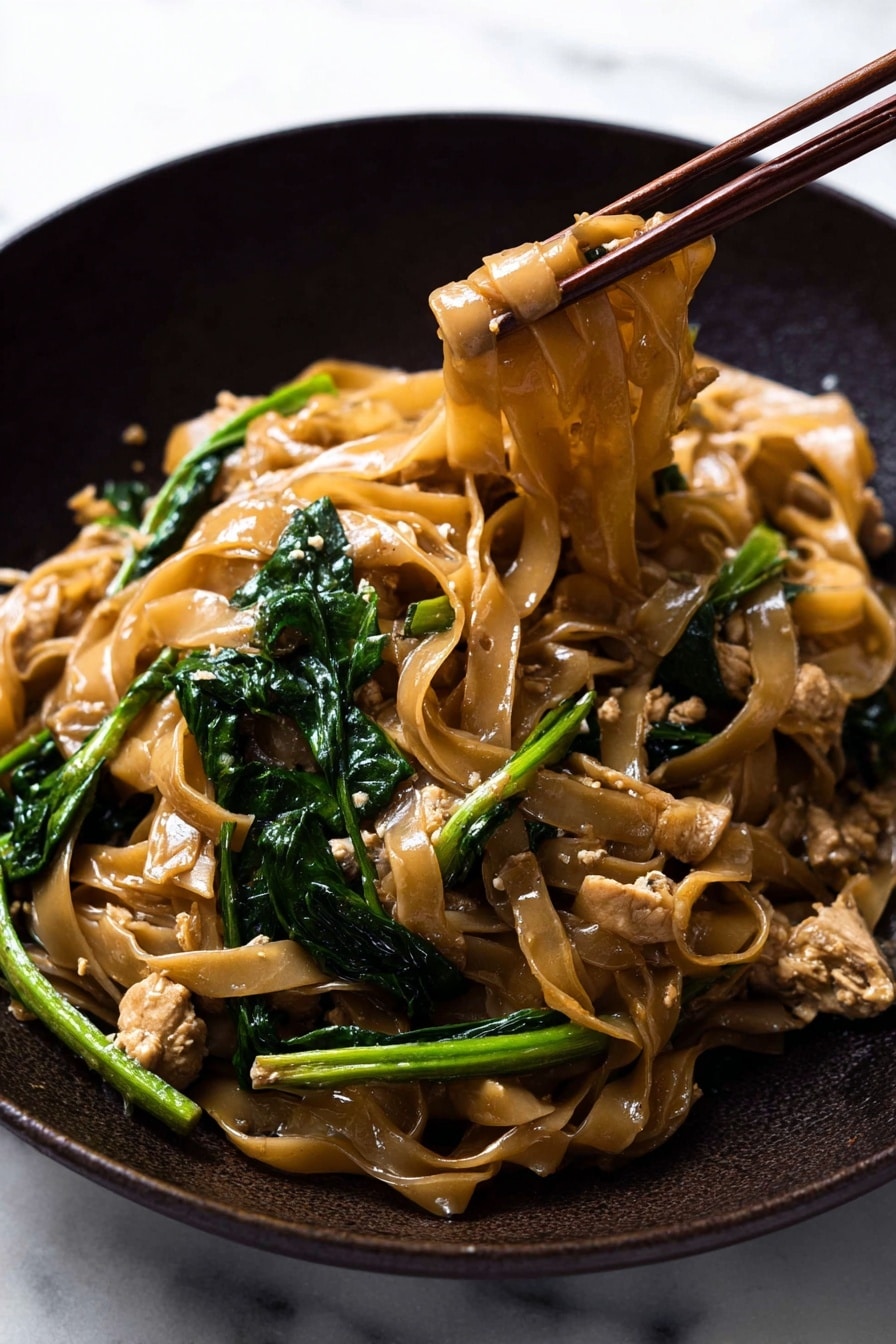 This image shows a close-up of stir-fried noodles in a dark pan. The dish has wide, flat noodles that are light brown and shiny from sauce, mixed with bright green leafy vegetables and light brown pieces of cooked chicken. The noodles and vegetables are tangled together, with the noodles forming the main layer in the center and the green vegetables scattered around. A wooden spatula is seen gently holding some of the noodles from the top right side. The background is a white marbled texture. photo taken with an iphone --ar 2:3 --v 7 - Easy Thai Pad See Ew Stir Fry, Thai Pad See Ew, Stir Fry recipes, Thai street food, quick Asian noodle dishes