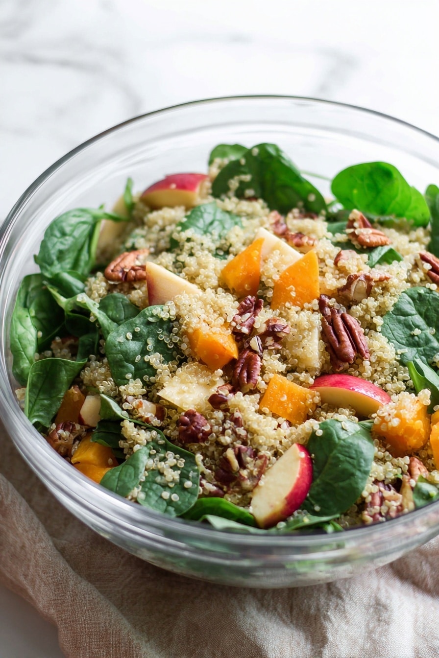 A clear glass bowl holds a salad with three main layers: a bottom layer of light beige quinoa grains scattered throughout, a middle layer of bright green fresh spinach leaves placed on top and mixed in, and a top layer consisting of medium-sized chunks of orange squash, small cubes of red and yellow apple pieces, light beige chickpeas, and whole brown pecan nuts arranged evenly around the salad. Next to the bowl is a small white bowl filled with pecans. The setting includes two vintage silver salad servers placed on a white and red striped cloth, all set on a white marbled texture surface. photo taken with an iphone --ar 2:3 --v 7 - Roasted Butternut Squash Quinoa Salad, healthy roasted squash salad, quinoa vegetable salad, seasonal fall salads, nutritious vegetarian salads