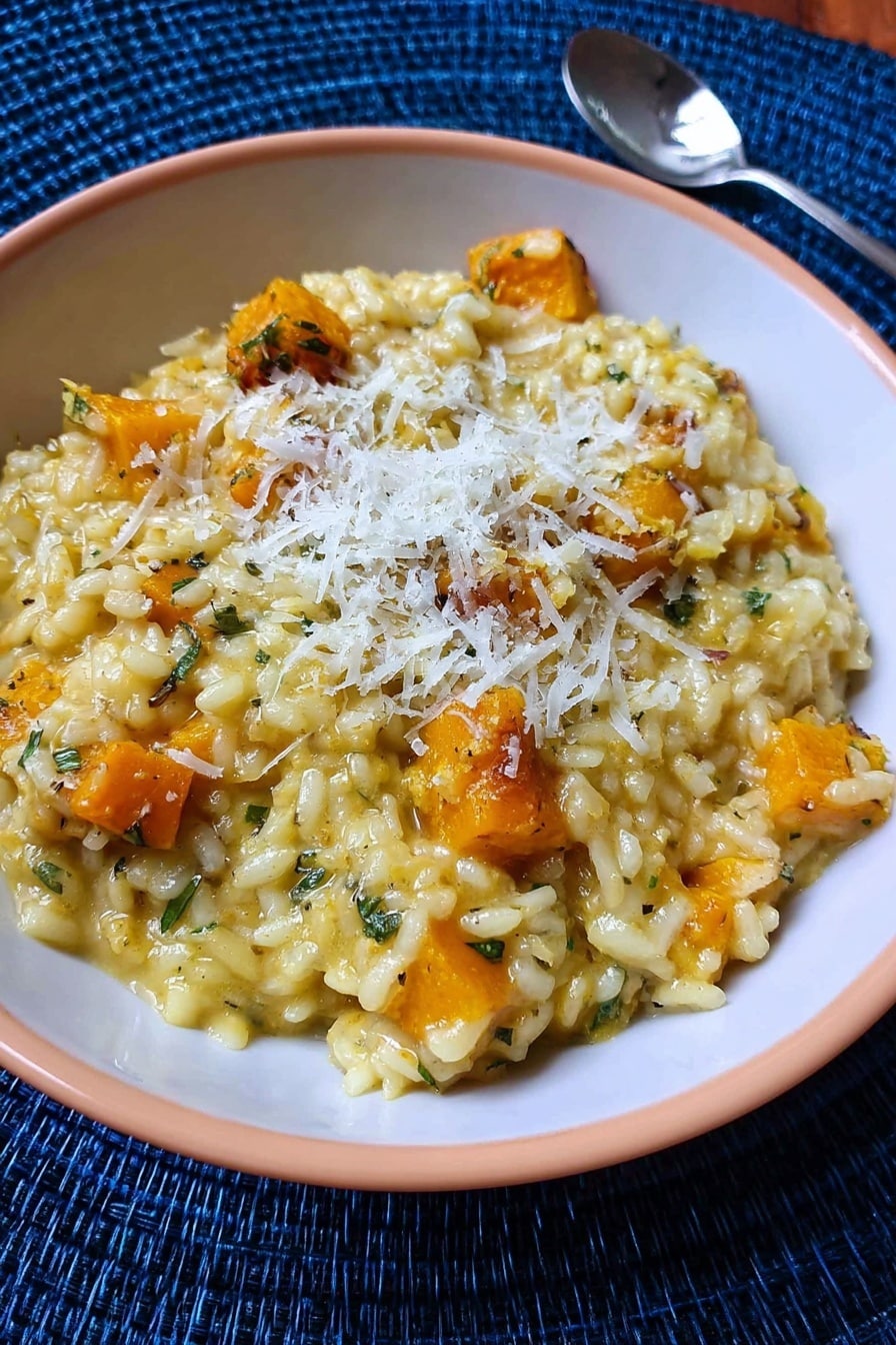 A white plate with blue patterns holds a layer of creamy yellow risotto with soft, slightly shiny grains and some orange pieces mixed inside. On top, there is a thick, juicy piece of cooked meat with a browned surface and visible herbs. A small green sprig of rosemary lies between the risotto and meat, adding fresh color. The plate is set against a white marbled background. photo taken with an iphone --ar 2:3 --v 7 - Butternut Squash Risotto with Saffron, creamy butternut squash risotto, saffron risotto recipes, vegetarian risotto ideas, cozy fall risotto