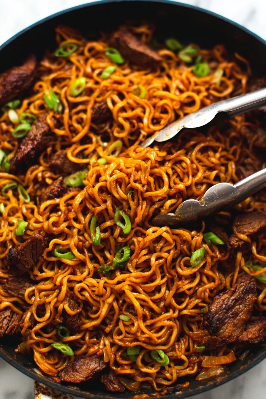 The image shows a close-up of a black pan filled with cooked noodles mixed with pieces of dark brown meat. The noodles are a warm orange-brown color, twisted and tangled together with small green onions sprinkled on top for color contrast. A pair of silver tongs is gripping some noodles and meat in the top right area of the pan. The pan sits on a white marbled surface. photo taken with an iphone --ar 2:3 --v 7 - Spicy Korean Beef Noodles, Korean Beef Noodles, Spicy Noodle Recipe, Korean Beef Stir-fry, Easy Korean Noodles