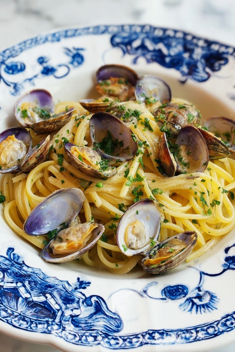 A white plate with blue floral patterns holds a serving of spaghetti pasta layered at the bottom, showing a pale yellow color and smooth texture. Scattered over the pasta are many opened clam shells, beige and light brown with tender clam meat inside, slightly orange and shiny. Fresh chopped green herbs are sprinkled over the clams and pasta, adding a bright touch. The plate rests on a white marbled surface. photo taken with an iphone --ar 2:3 --v 7 - Linguine with Clams, clam linguine recipe, Italian pasta with clams, easy seafood pasta, briny garlic pasta