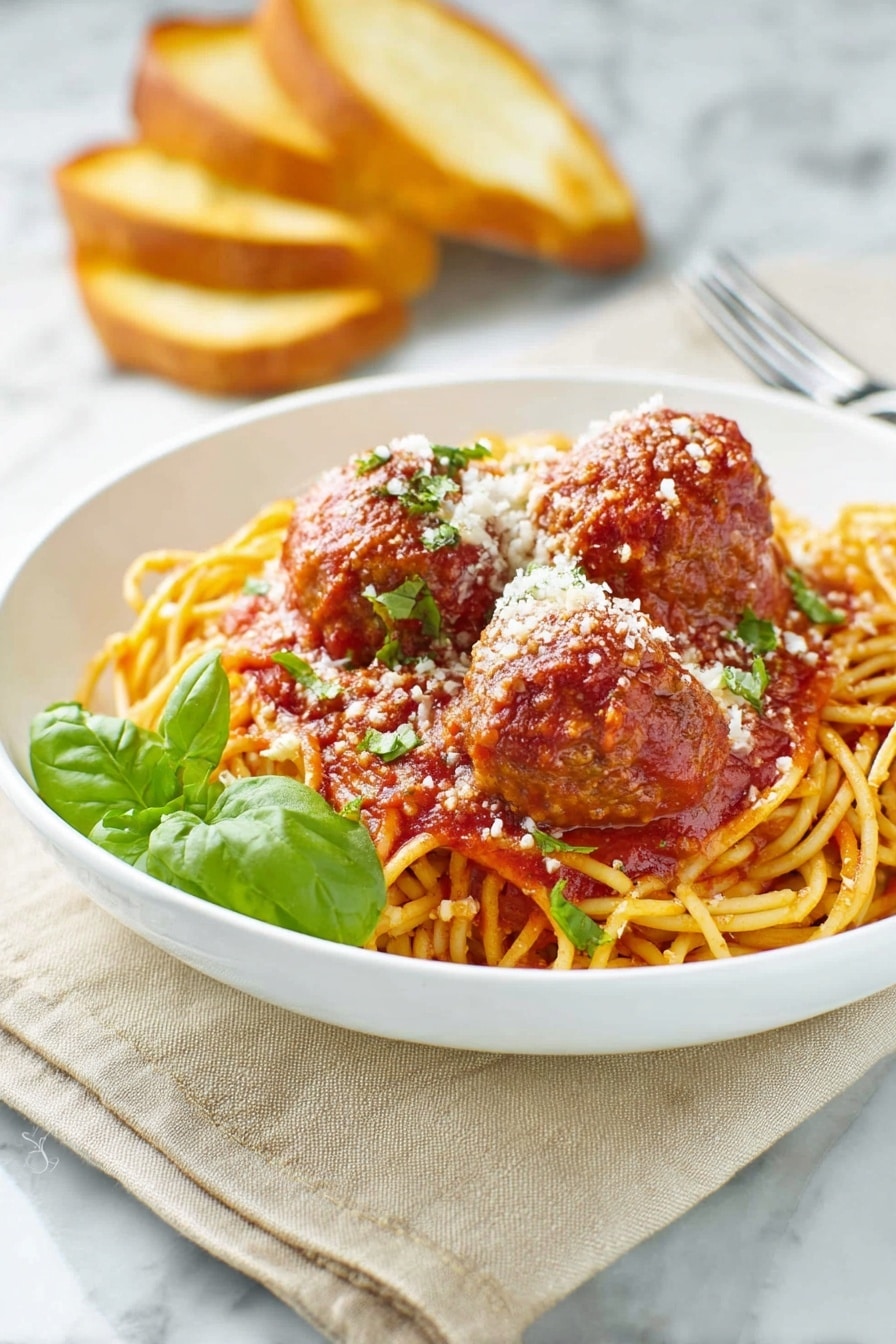A white bowl holds a bed of golden-yellow spaghetti noodles topped with rich red tomato sauce. On top, there are three large brown meatballs coated in the sauce, sprinkled with white grated cheese and small green herb pieces. A fresh green basil leaf adds color near the front. In the background, there are three toasted bread slices leaning against the bowl. The scene sits on a beige cloth over a white marbled surface. A silver fork rests nearby on the right side. Photo taken with an iphone --ar 2:3 --v 7 - Homemade Spaghetti and Meatballs, Italian pasta with meatballs, easy spaghetti and meatballs, classic Italian spaghetti dish, homemade marinara and meatballs