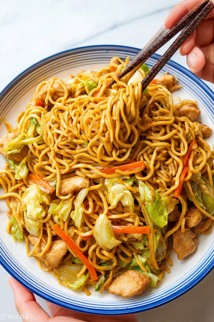 A white plate with a blue rim holds a serving of stir-fried noodles mixed with pieces of cooked light brown chicken, bright orange carrot sticks, and green cabbage leaves. The noodles are golden yellow and tangled together, with some lifted by dark brown chopsticks held by a woman's hand above the plate. The plate is on a white marbled surface, and the woman’s hand is seen at the bottom left corner holding the plate slightly. Photo taken with an iphone --ar 2:3 --v 7 - Easy Chicken Yakisoba Stir-Fry, Chicken Yakisoba, Japanese stir-fry, quick dinner ideas, savory noodle recipes