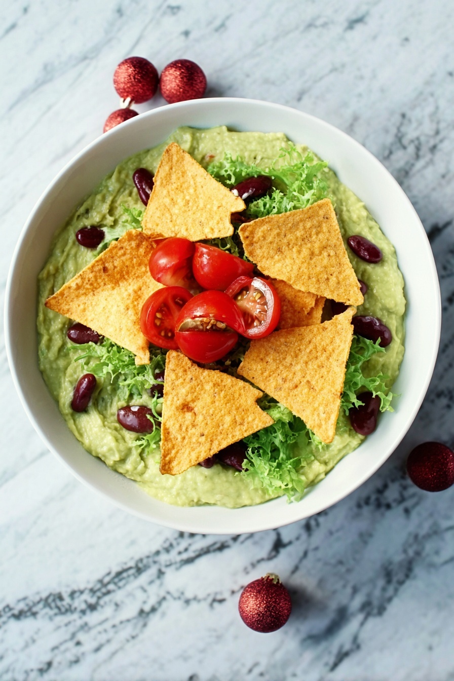 A white bowl filled with a creamy green guacamole base topped by several crispy golden tortilla chips placed in the center. Around the chips, there are bright red cherry tomato halves, fresh green lettuce leaves, and small dark red kidney beans scattered. The bowl is set on a white marbled surface. photo taken with an iphone --ar 2:3 --v 7 - Festive Guacamole with Pomegranate & Tomatoes, holiday guacamole, colorful party dip, easy holiday appetizer, quick festive salsa