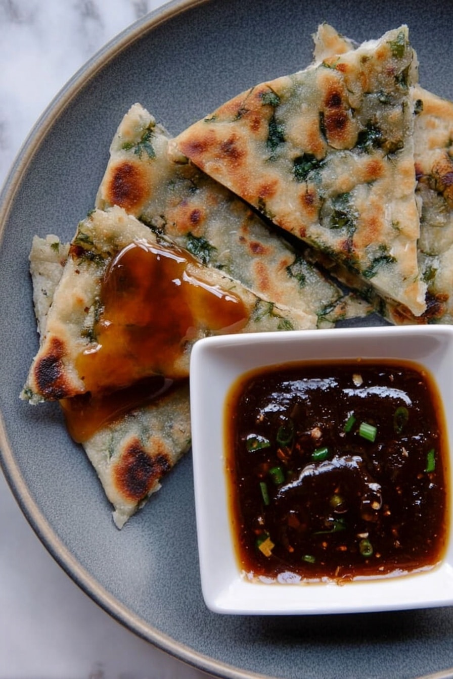 The image shows a close-up of a grey plate on a white marbled surface, with four triangular pieces of flatbread that have green herbs inside, each piece varying in size and texture with some browned spots from cooking. One piece near the bottom left has a shiny layer of sticky, dark amber sauce on top. To the right, a small white square bowl holds a thick, dark brown dipping sauce with small green bits inside, creating a glossy surface. photo taken with an iphone --ar 2:3 --v 7 - Chinese Scallion Pancakes, how to make scallion pancakes, crispy scallion pancakes, Chinese street food recipes, homemade scallion pancakes