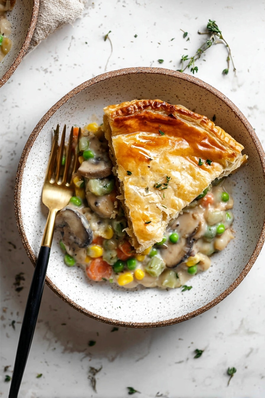 The dish shows one slice of golden brown pastry with a shiny and slightly cracked top crust, placed on top of a creamy mixture with visible layers of light green celery, orange carrot pieces, yellow corn, green peas, white beans, and brown mushrooms. The mix is thick and creamy with small bits of herbs sprinkled on top. The food is served in a white bowl with speckled details, alongside a black and gold fork resting inside the bowl on the left side. The background is a white marbled surface with scattered small green herbs. Photo taken with an iphone --ar 2:3 --v 7 - Creamy Vegetable Pot Pie, vegetable pot pie recipe, vegetarian pot pie, cozy vegetable pie, easy creamy pot pie