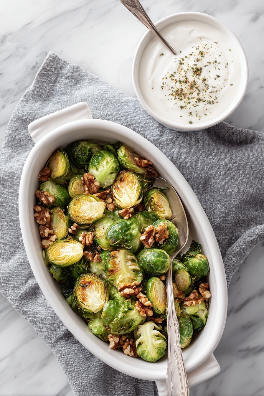 A white oval dish filled with two layers of roasted Brussels sprouts that are deep green with golden brown edges, topped with scattered light brown walnut halves. A silver spoon rests inside the dish, partially submerged in the vegetables. The dish sits on a gray cloth napkin with a white marbled background. To the right, there is a small white bowl filled with white creamy sauce topped with a sprinkling of brown herbs, with a white spoon inside. Photo taken with an iphone --ar 2:3 --v 7 - Roasted Brussels Sprouts with Walnuts and Pomegranate, Brussels Sprouts Side Dish, Pomegranate and Walnut Veggie Recipe, Healthy Brussels Sprouts Ideas, Easy Roasted Brussels Sprouts