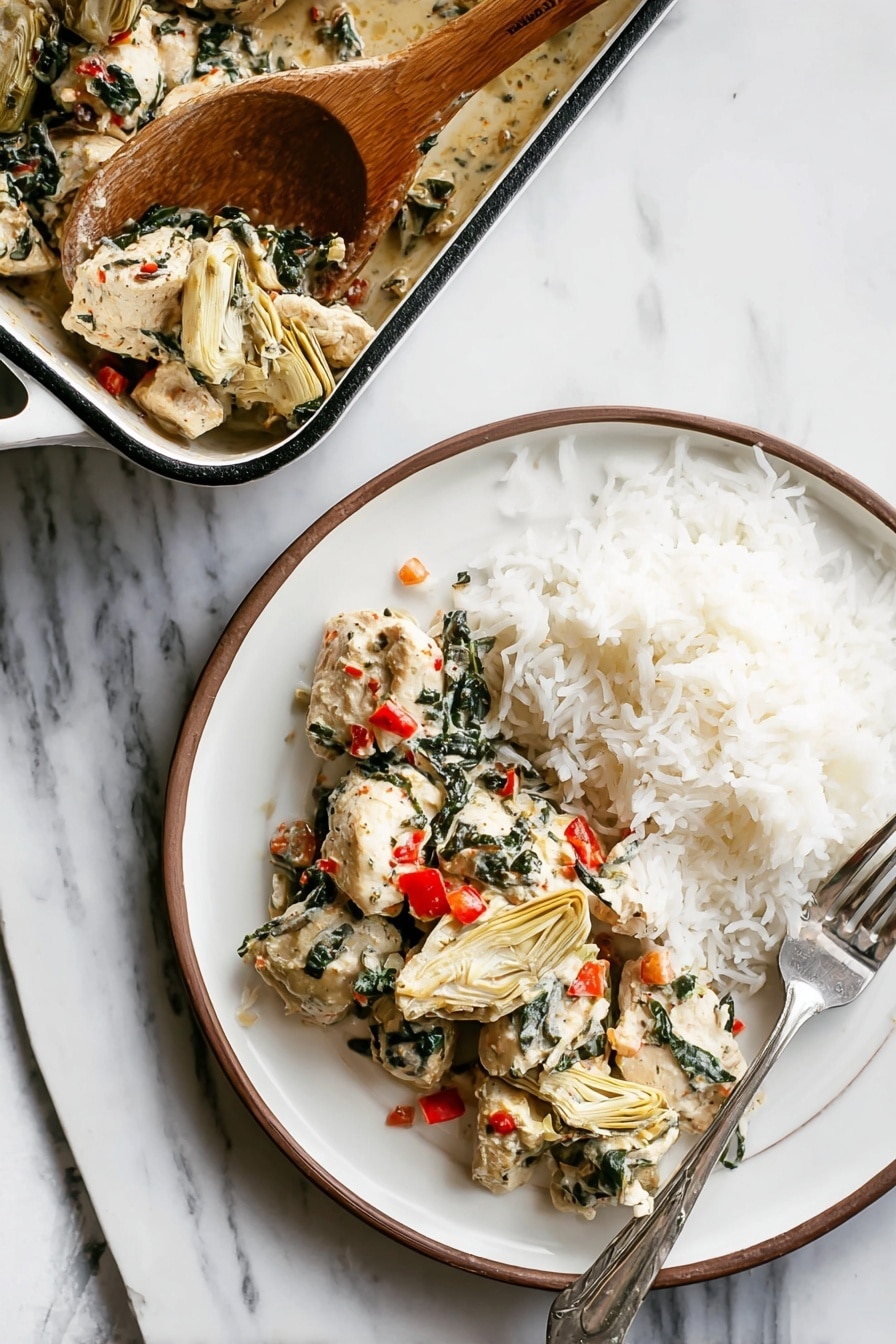 A white round plate shows two layers: on the left side, there are pieces of white cooked chicken mixed with dark green spinach leaves and small bright red bits of bell pepper, along with beige artichoke hearts placed among the chicken; on the right side, there is a mound of fluffy white rice with a silver fork resting on the right edge of the plate. Above the plate, a white rectangular baking dish with a dark rim holds more chicken mixture, and a wooden spoon is scooping some of the chicken and vegetables from the dish. All items are placed on a white marbled surface. photo taken with an iphone --ar 2:3 --v 7 - Spinach Artichoke Chicken Bake, creamy chicken bake with spinach and artichokes, easy chicken dinner recipes, one-pan chicken dish, healthy chicken bake ideas