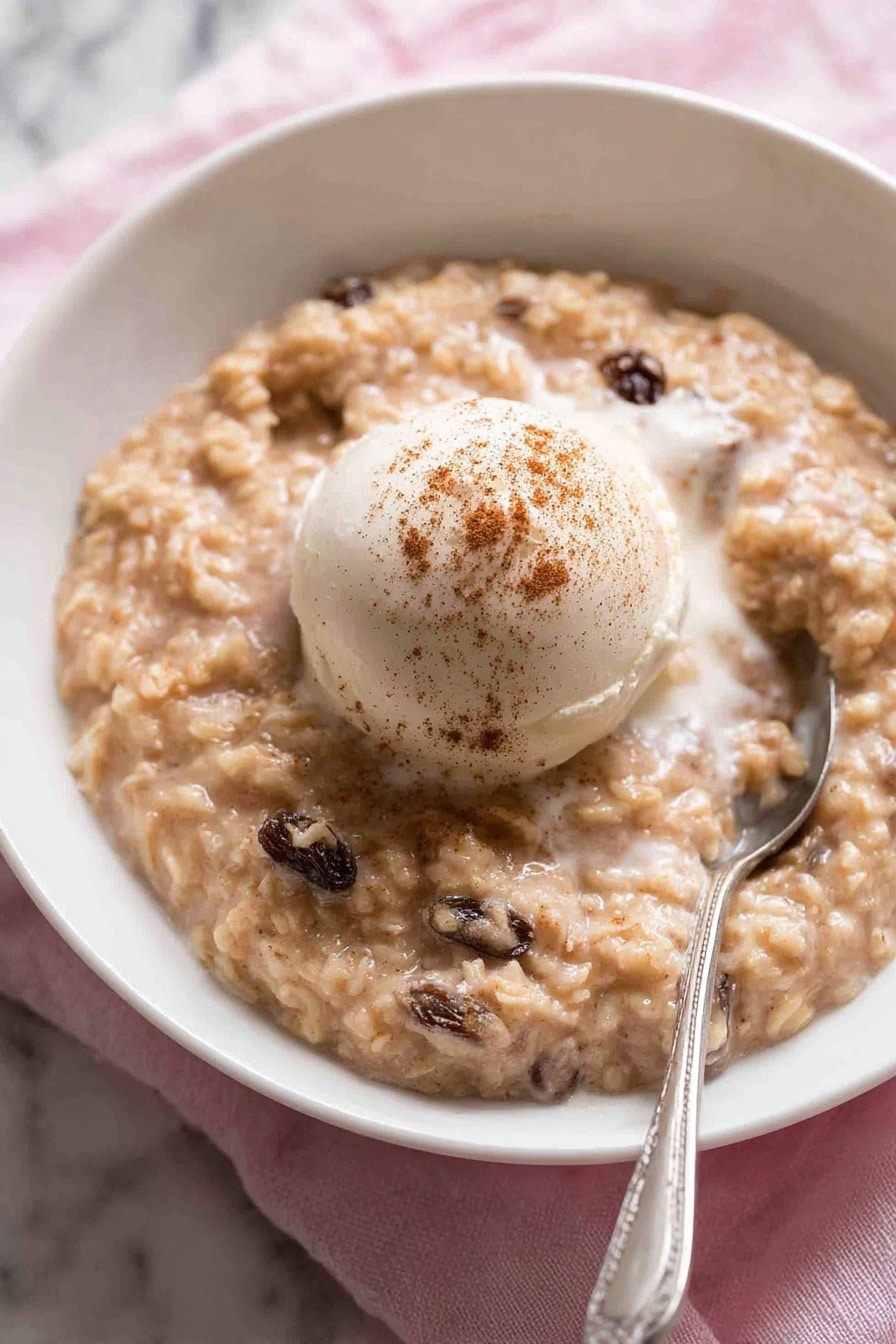The image shows three white ceramic bowls filled with a creamy dessert that has a beige color with visible raisins mixed in. Each bowl has a smooth, round scoop of white ice cream on top, sprinkled lightly with brown cinnamon powder. The dessert looks thick and slightly textured, with a soft, milky sauce layering part of the surface around the ice cream. The bowls are placed on a soft gray cloth, set on a white marbled surface. One bowl is in the front and in clear focus, while the other two are placed slightly behind and blurred. A white spoon is placed on the cloth next to the front bowl. photo taken with an iphone --ar 2:3 --v 7 - Creamy Cinnamon Rice Pudding, rice pudding with cinnamon, easy rice pudding recipe, cozy dessert with raisins, baked rice pudding