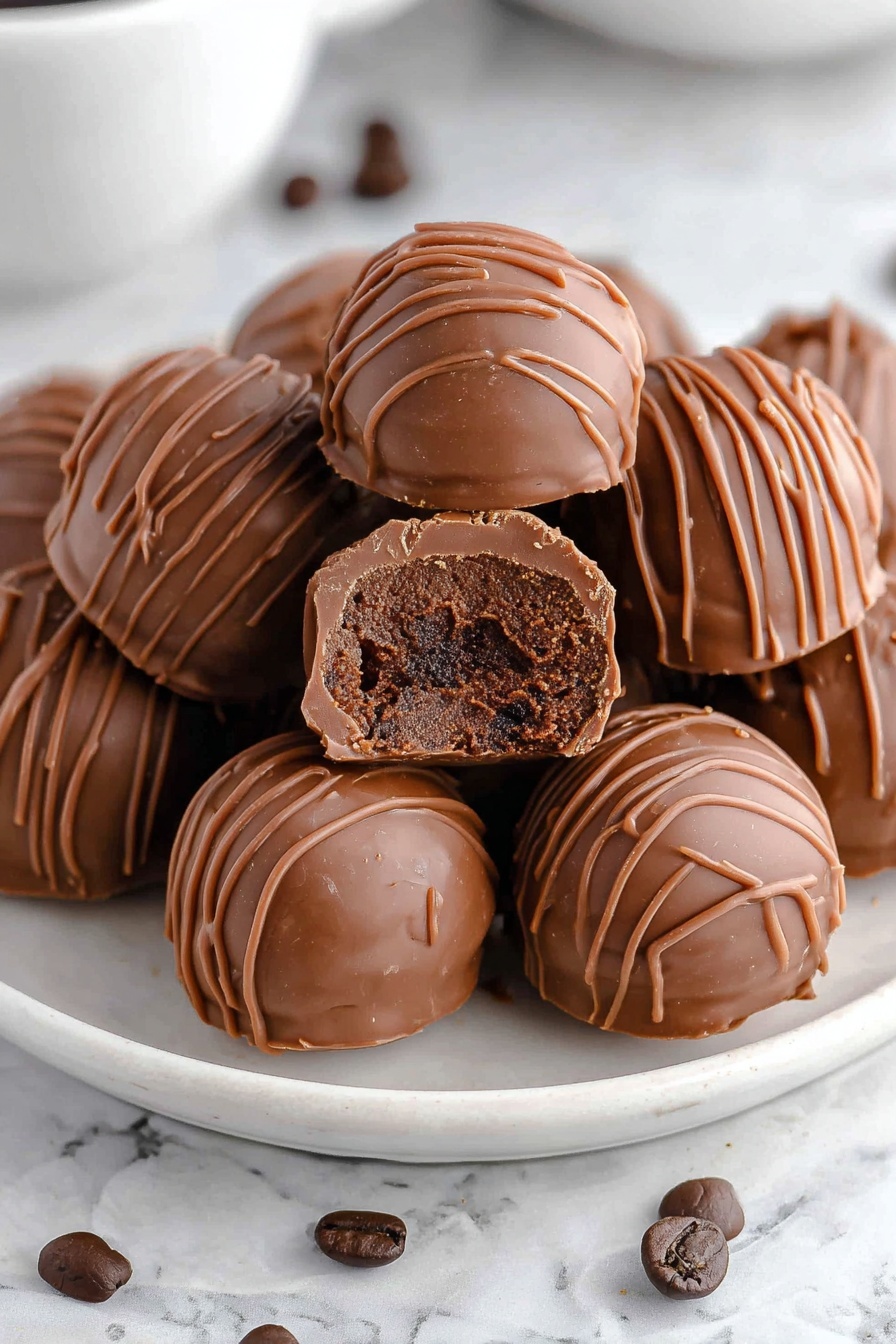 A white plate filled with round milk chocolate truffles, each truffle covered with thin milk chocolate drizzle lines on top. One truffle is broken in half and placed on top of the others, showing a thick, darker chocolate center with a smooth and slightly crumbly texture inside. The plate is on a white marbled surface with a few dark brown coffee beans scattered around. Photo taken with an iphone --ar 2:3 --v 7 - Coffee Chocolate Truffles, coffee chocolate dessert, easy chocolate truffles, decadent coffee treats, homemade coffee truffles