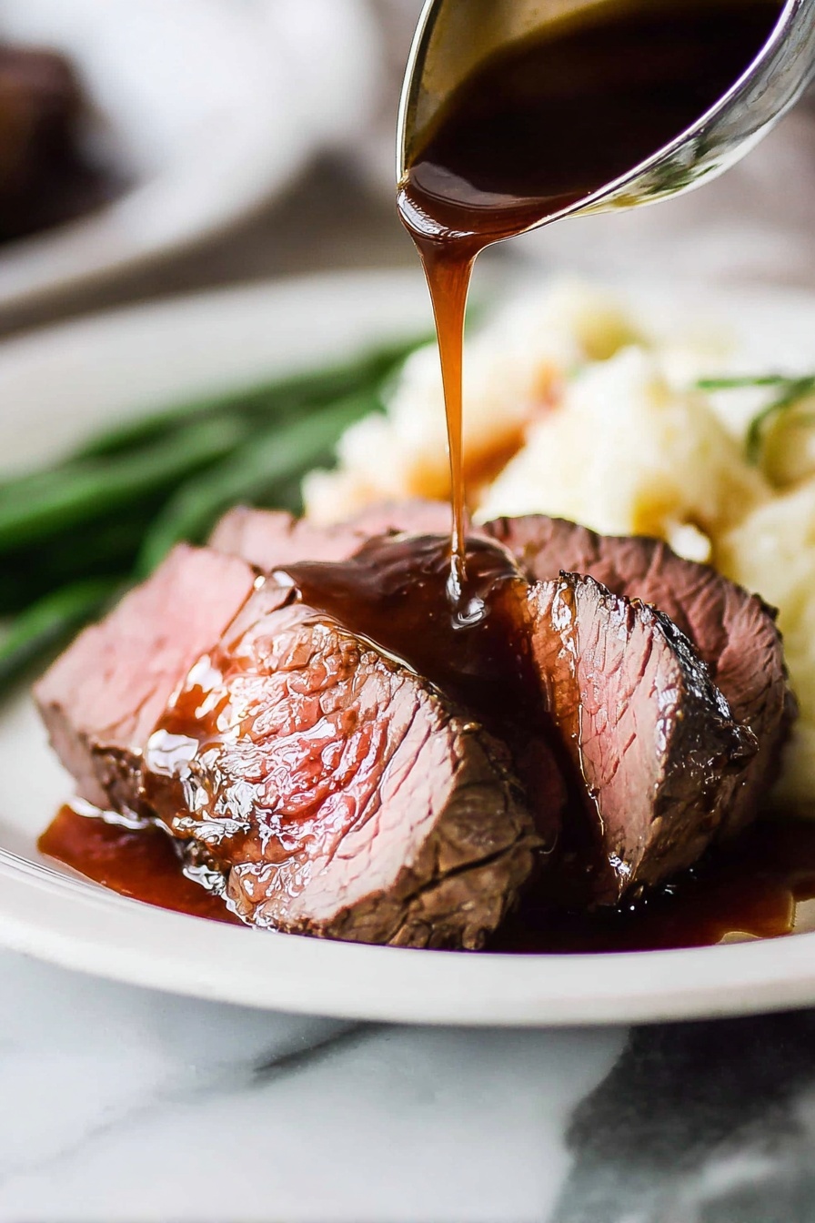 The image shows two thick slices of medium-rare roast beef placed on a white plate with a white marbled surface in the background. The roast beef has a brown crust on the outside and a pink center. A dark brown gravy sauce is being poured over the top slice from a ladle, creating a shiny texture with some sauce pooling on the plate. Behind the beef, there is a serving of creamy mashed potatoes and a few green beans slightly blurred in the background. The focus is on the meat and sauce with a close-up view emphasizing the moist texture of the beef and the rich shine of the gravy. Photo taken with an iphone --ar 2:3 --v 7 - Beef Tenderloin with Red Wine Sauce, fancy beef dinner, gourmet beef recipe, easy red wine sauce, special occasion beef dish