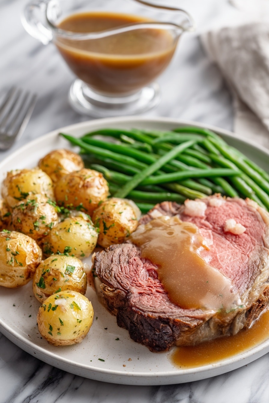 A white plate on a white marbled surface holds a meal with three main parts: a thick, medium-rare roast beef slice with a pink center and browned edges, topped with brown gravy that also pools around it; next to it, a pile of roasted small potatoes with golden brown skins sprinkled with green herbs; and a bunch of bright green cooked green beans laid neatly beside the potatoes. In the background, there is a clear glass gravy boat filled with brown gravy on the white marbled surface. photo taken with an iphone --ar 2:3 --v 7 - Garlic Herb Butter Prime Rib, prime rib roast with garlic and herbs, best prime rib recipe, holiday prime rib, juicy prime rib dinner