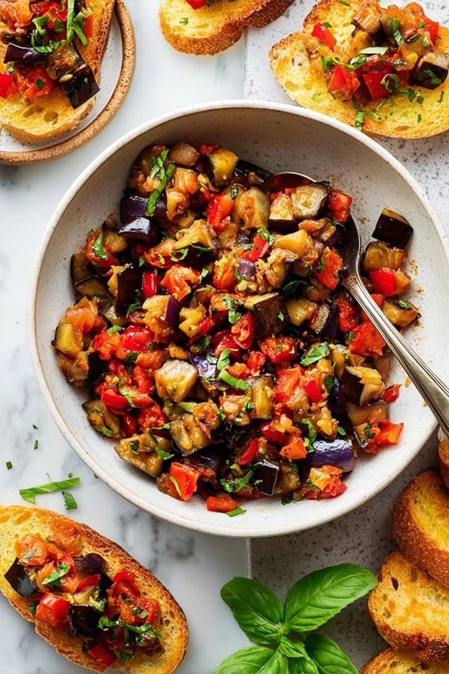 A white bowl filled with a colorful mix of roasted vegetables, mostly deep purple eggplants and bright red bell peppers, chopped into small pieces and mixed with finely chopped green herbs sprinkled on top. A silver spoon rests inside the bowl with its handle leaning on the edge. Around the bowl, there are toasted slices of bread topped with the same vegetable mix, placed on a white marbled surface. Fresh green basil leaves add a pop of color near the bowl. The overall look is fresh and vibrant, with a mix of soft cooked texture and crunchy toasted bread. photo taken with an iphone --ar 2:3 --v 7 - Eggplant Caponata, Eggplant Caponata recipe, Sicilian eggplant dish, flavorful eggplant appetizer, tangy eggplant stew
