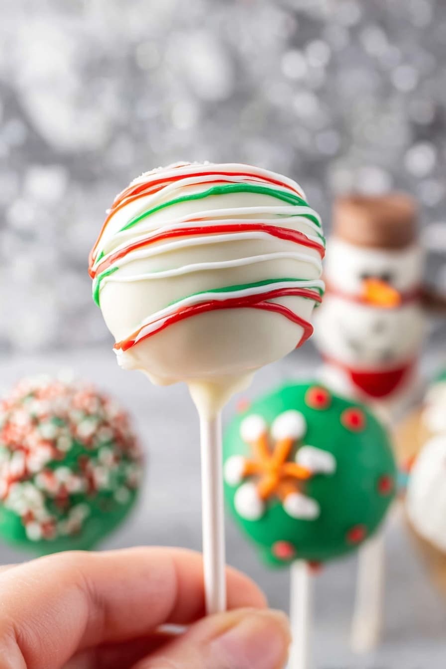 A white round cake pop on a white stick is held by a woman's hand in the foreground. The cake pop has a smooth white coating with thin lines of red and green icing drizzled around it in a spiral pattern. In the blurred background, there are other festive cake pops with different decorations, including green coating with sprinkles and shapes that resemble snowmen with orange and red details. The scene is set against a white marbled surface with a soft silver sparkly backdrop. Photo taken with an iphone --ar 2:3 --v 7 - Christmas Cake Pops, holiday cake pops, festive dessert treats, easy Christmas treats, bite-sized holiday desserts