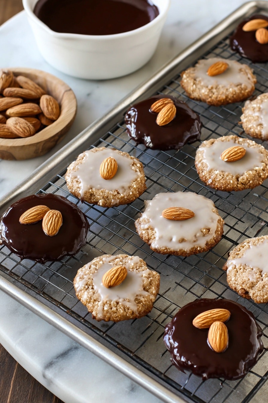 The image shows a metal cooling rack on a baking tray with two types of round cookies. The first type has a light glaze coating, making the cookie slightly shiny white, with three whole almonds arranged in a triangle shape on top. The other type is covered in a smooth, glossy dark chocolate layer, with three whole almonds arranged the same way on top. The tray sits on a white marbled surface. In the background, a white bowl holds more melted dark chocolate. photo taken with an iphone --ar 2:3 --v 7 - German Lebkuchen, Lebkuchen with Chocolate Glaze, German holiday cookies, traditional German gingerbread, spiced gingerbread cookies