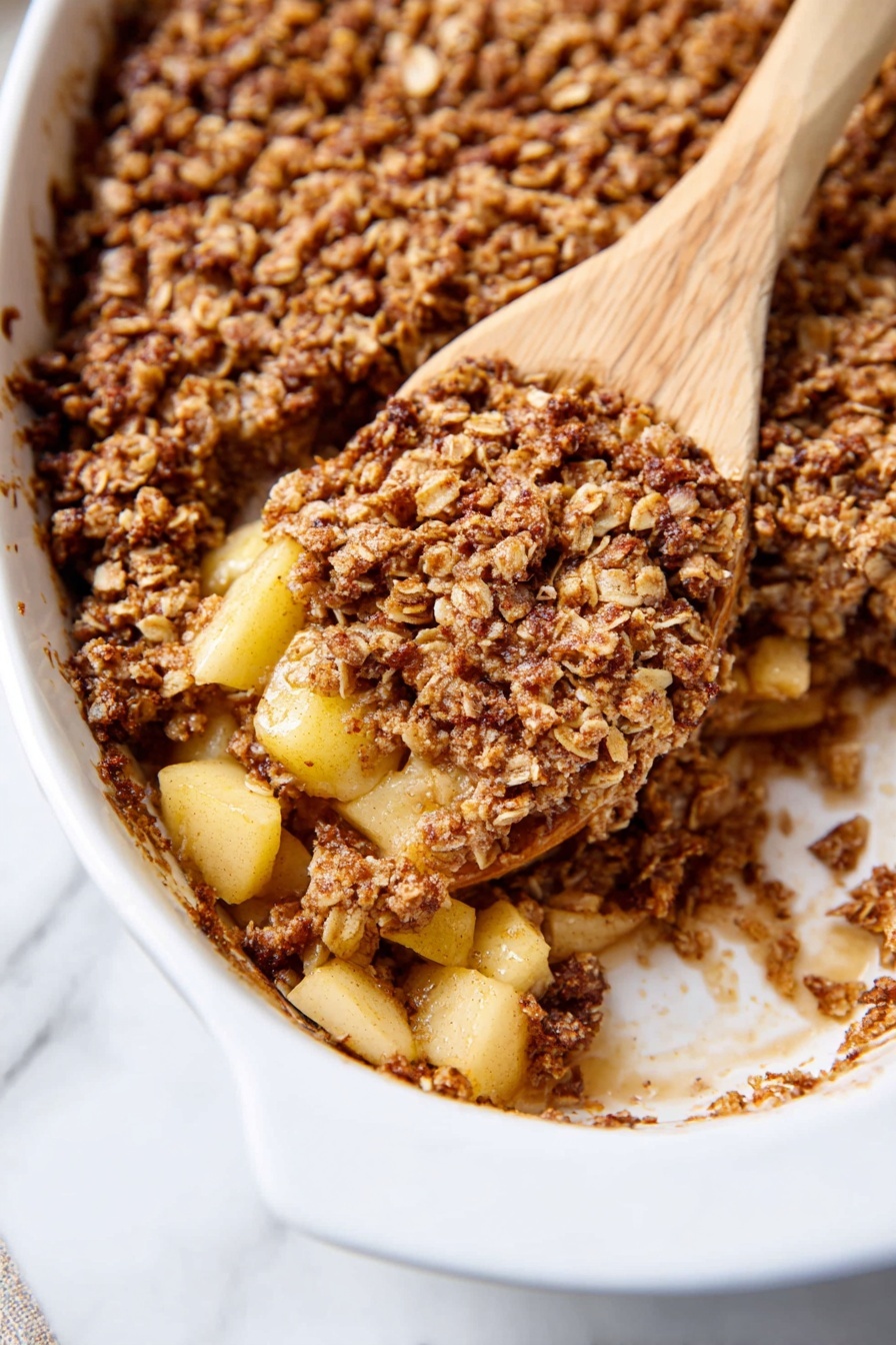 The image shows a white oval baking dish filled with a baked oatmeal dish. The top layer is a golden brown, crumbly oat mix with visible oats and a rough texture. Underneath, chunks of soft, light yellow cooked apple pieces are mixed within the oat mixture, giving a chunky and moist look. A wooden spatula is scooping a portion from the dish, showing the thick and hearty inside with bits of oats and apples combined. The white dish has some brown baked bits around its edge, and the dish is set on a white marbled surface. Photo taken with an iphone --ar 2:3 --v 7 - Cinnamon Apple Baked Oatmeal, healthy baked oatmeal with apples, cozy breakfast ideas, easy make-ahead breakfast recipes, nourishing oatmeal breakfast