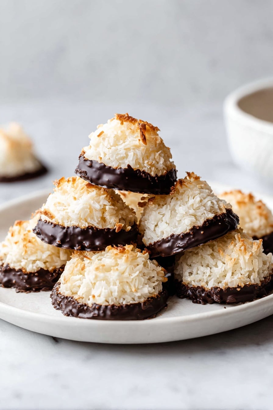A white plate holds eight dome-shaped coconut macaroons, each with a lightly toasted top and dipped in a thick layer of dark chocolate at the bottom. The macaroons have a rough, shredded coconut texture on the top two-thirds and the smooth, shiny chocolate coating neatly covers the lower third. Three macaroons are stacked in the center, and the rest are arranged around them on the white marbled surface. A bit of white bowl is seen blurred in the background. Photo taken with an iphone --ar 2:3 --v 7 - German Coconut Macaroons, coconut macaroon recipe, tropical cookies, easy coconut cookies, kokosmakronen