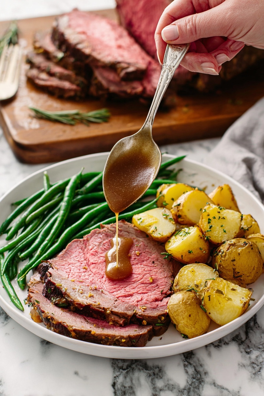 A white plate holds a meal with three layers: a large slice of pink roast beef with a browned edge forms the base layer, topped with bright green cooked green beans arranged in a neat pile along one side, and golden roasted potato chunks with herbs sit next to the green beans. A woman's hand holds a silver spoon above the beef, pouring rich brown gravy directly onto the meat. In the background, a wooden board with a large piece of roast beef resting on it is visible against a white marbled surface. Photo taken with an iphone --ar 2:3 --v 7 - Perfect Garlic Herb Prime Rib, garlic herb prime rib, prime rib recipe, savory roast beef, holiday prime rib