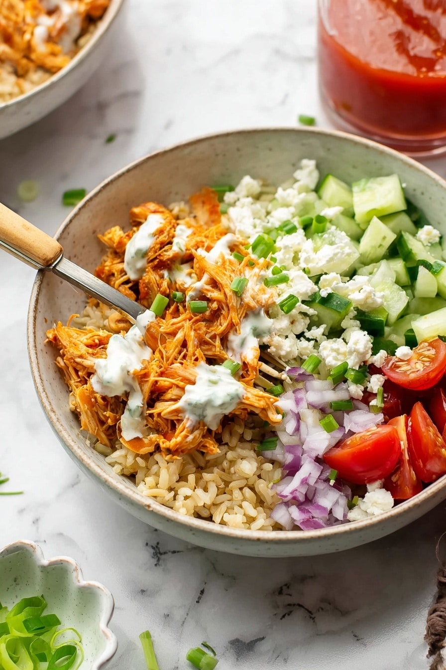 A bowl with four clear layers on a white marbled surface. The bottom layer is light brown rice forming a base. On one side, there is shredded orange chicken layered thickly over the rice. Above the chicken and rice, white creamy sauce is drizzled lightly. On the opposite side of the bowl, there are diced green cucumbers mixed with small bits of white cheese, purple onion pieces, and halved red cherry tomatoes. Some chopped green onions are scattered on top, adding a fresh green accent. A metal fork with a light brown handle is inside the bowl with shredded chicken on it. Behind the bowl, a clear glass with red sauce is visible, slightly out of focus, and a small white dish with sliced green onions is on the left side. photo taken with an iphone --ar 2:3 --v 7 - Buffalo Chicken Rice Bowls, buffalo chicken meal, easy rice bowl recipes, healthy chicken dinner, quick protein-packed meals