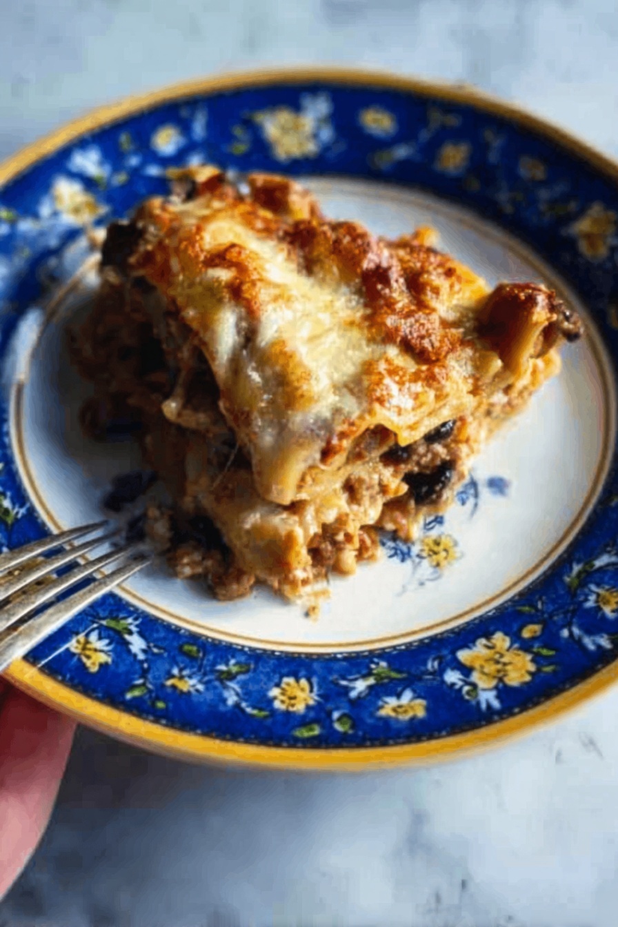 The image shows a close-up of a white plate with a blue and yellow floral pattern around the edge, holding a layered slice of lasagna. The lasagna slice has visible layers of browned melted cheese on top, a rich tomato sauce with ground meat and mushrooms below, followed by pale pasta sheets in between. A woman's hand with a fork is positioned to the side, ready to take a bite. The plate is on a white marbled surface. photo taken with an iphone --ar 2:3 --v 7 - Vegetarian Hatch Chile Enchiladas, Hatch Chile Enchiladas, Vegetarian Enchiladas with Hatch Chiles, Spicy Hatch Chile Vegetarian Dinner, Easy Vegetarian Hatch Chile Recipes