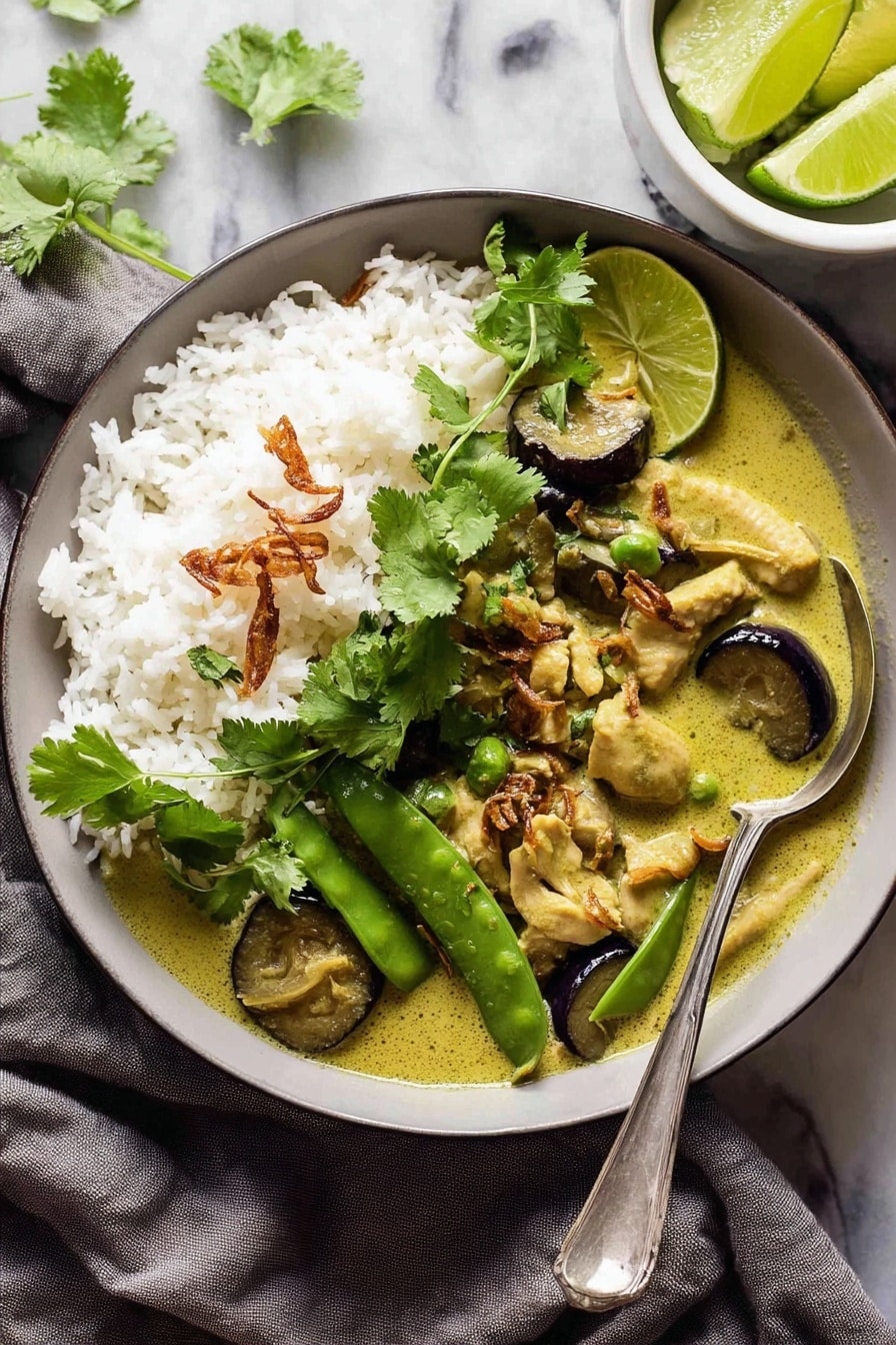 The image shows a black bowl filled with a creamy green curry dish. On the left side, there is a mound of white rice with a few crispy fried shallots sprinkled on top and a small bunch of fresh green cilantro leaves as garnish. The curry has thick slices of dark purple eggplant and fresh green snap peas floating in the light green sauce. A spoon is partially submerged in the curry on the right side of the bowl. The bowl is placed on a soft gray cloth with a small white plate with lime wedges and cilantro at the top right corner, all set on a white marbled surface. Photo taken with an iphone --ar 2:3 --v 7 - Authentic Thai Green Curry, Thai Green Curry Recipe, Thai Curry Dinner, How to Make Thai Green Curry, Spicy Thai Green Curry