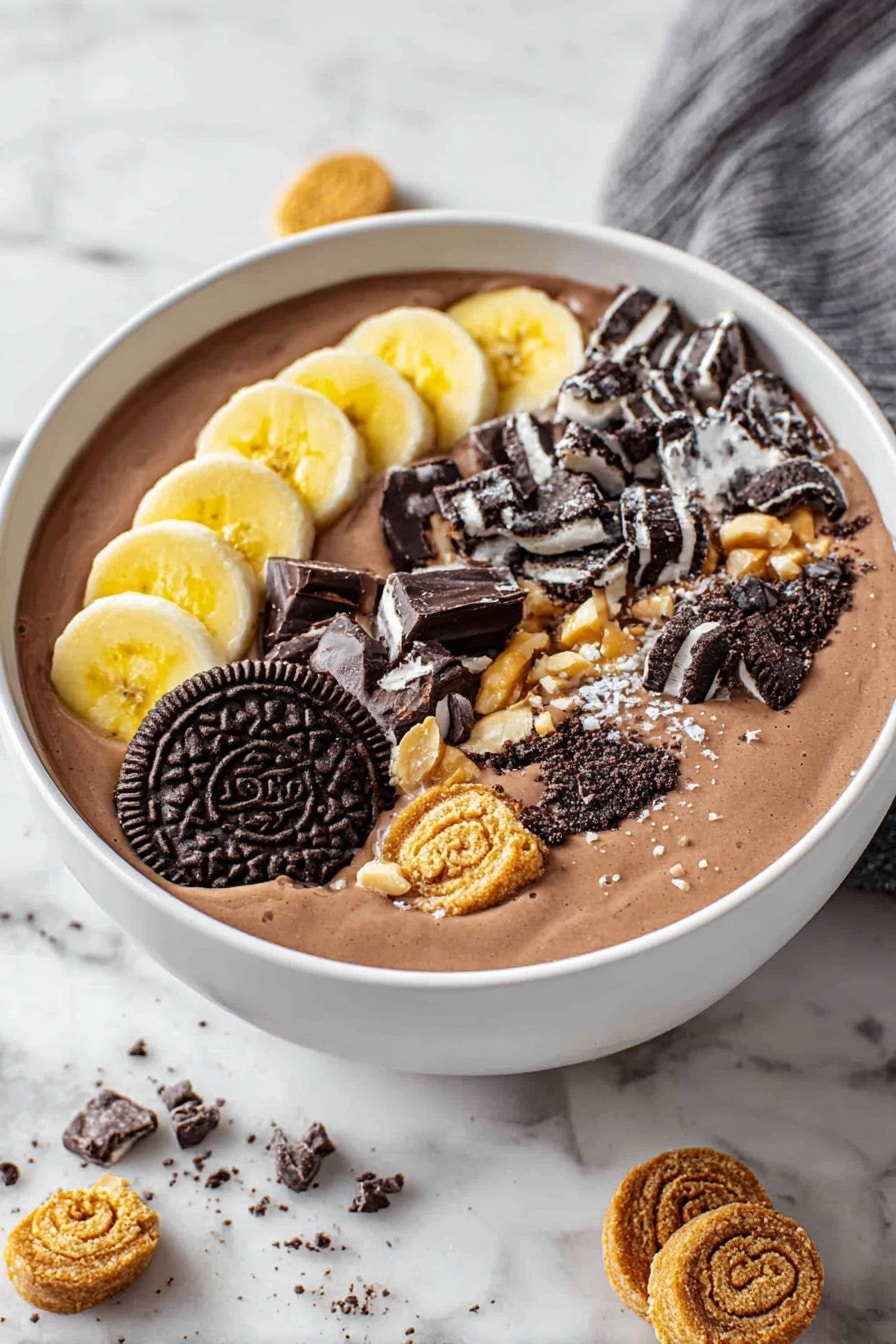 A white bowl filled with smooth, creamy chocolate smoothie as the base layer. On top, there are four rows of toppings: on the left, thin slices of bright yellow banana neatly arranged; next to it, broken pieces of dark chocolate with nuts inside; beside that, scattered chunks of black and white sandwich cookies; and to the far right, sliced pieces of a crunchy caramel nut roll. The bowl sits on a white marbled surface with some cookie crumbs and dark chocolate chips scattered around. Photo taken with an iphone --ar 2:3 --v 7 - Chocolate Banana Smoothie Bowl, healthy smoothie bowl recipes, quick breakfast ideas, indulgent yet healthy breakfast, banana smoothie bowl