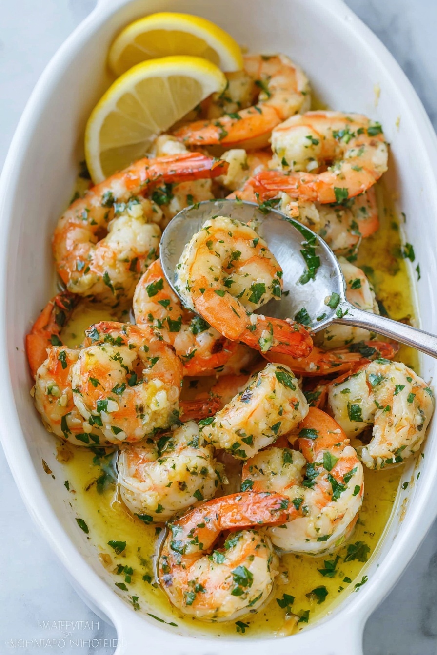 In a white oval dish filled with plump cooked shrimp, the shrimp are arranged in a loose pile with orange-pink tails curled and white meaty bodies showing. They are coated in a glossy yellow garlic butter sauce mixed with bright green chopped herbs scattered on top and mixed throughout. A silver spoon inside the dish holds several shrimp, partially covered in sauce, as two lemon wedges sit beside the dish on a white marbled surface. The shrimp have a lightly browned texture and there are small bits of garlic visible on them. Photo taken with an iphone --ar 2:3 --v 7 - Quick Garlic Shrimp Scampi, garlic shrimp dinner, easy shrimp recipes, quick seafood dishes, flavorful shrimp scallop