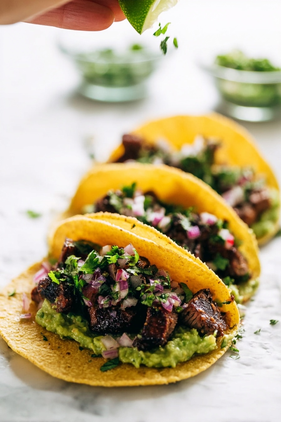 Three tacos are lined up on a white marbled surface, each taco made with a yellow corn tortilla that holds several layers. The bottom layer is chunky green guacamole, topped with small pieces of grilled dark brown meat with a slightly charred texture. Sprinkled over the meat are small bits of fresh green cilantro and finely chopped pinkish-red onions. Above the tacos, a woman's hand is squeezing a fresh lime wedge, adding a bright green color and a juicy texture to the scene. The background is softly blurred with clear glass bowls holding more chopped herbs and onions. Photo taken with an iphone --ar 2:3 --v 7 - Marinated Mojo Steak Tacos, flavorful steak tacos, quick guacamole recipe, citrus marinade steak, easy taco dinner ideas