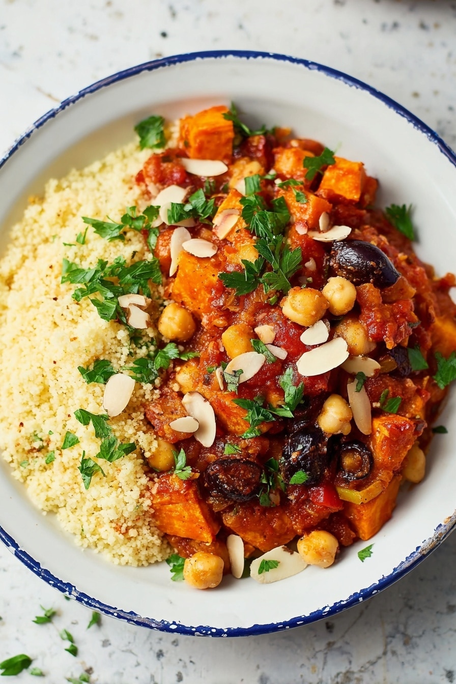 A white bowl filled with two main layers: the bottom layer is light yellow couscous with a fluffy, grainy texture covering half of the bowl; on top is a colorful stew made of dark orange chunks of roasted sweet potatoes, light brown chickpeas, and deep purple olives, all mixed in a rich, chunky red tomato sauce scattered with green parsley leaves and topped with thin, light beige almond slices. The bowl sits on a white marbled surface with a silver fork and green herb leaves in the blurred background. Photo taken with an iphone --ar 2:3 --v 7 - Moroccan Chickpea Stew with Sweet Potatoes, hearty Moroccan chickpea stew, flavorful vegan stew, spicy sweet potato and chickpea recipe, healthy Moroccan vegetarian dish