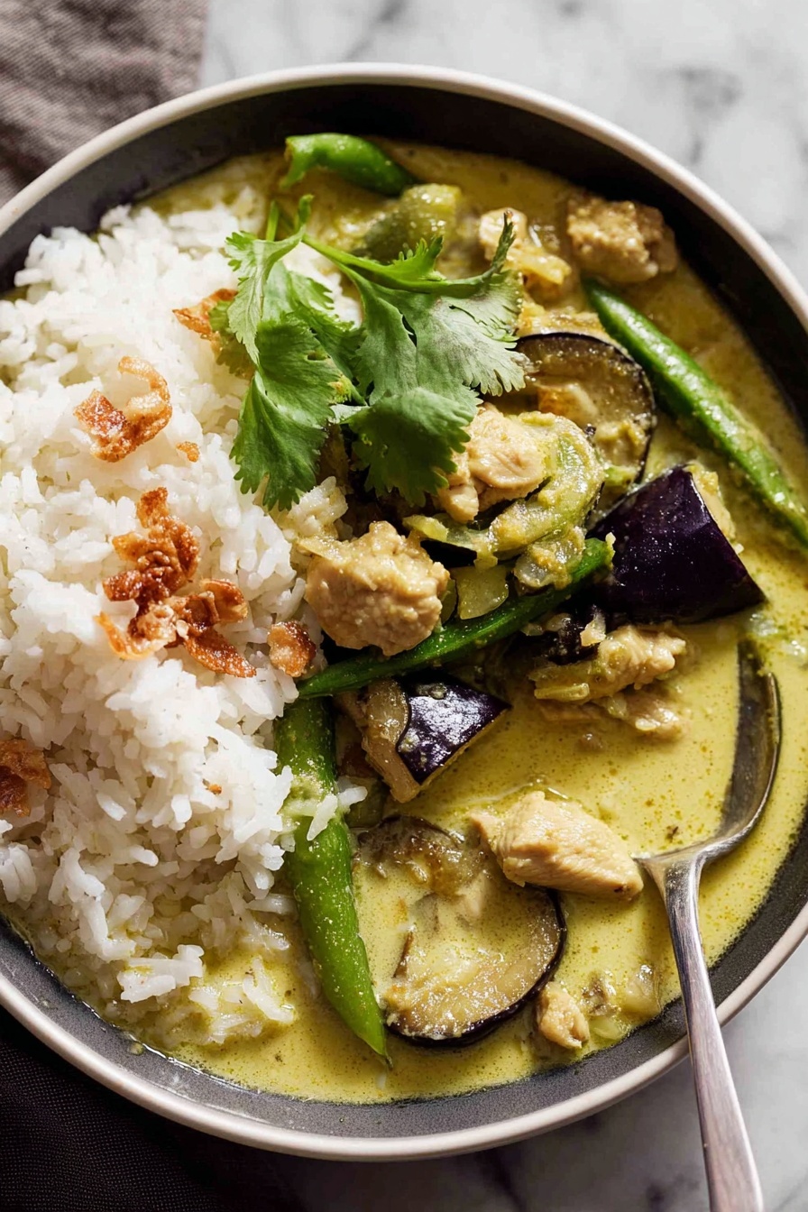 A white bowl filled with two main layers: on one side, a mound of plain white rice with a sprig of fresh green cilantro on top, and on the other side, creamy green curry sauce with pieces of soft green eggplant slices, light green sugar snap peas, tender chunks of chicken, and some golden crispy fried shallots scattered on top. A silver spoon rests inside the curry, partly lifting some rice and sauce. The bowl sits on a white marbled surface, and there is a soft brown cloth partly visible in the background. Photo taken with an iphone --ar 2:3 --v 7 - Authentic Thai Green Curry, Thai Green Curry Recipe, Thai Curry Dinner, How to Make Thai Green Curry, Spicy Thai Green Curry