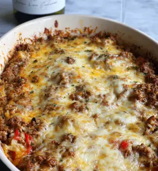 A close-up view of a white oval baking dish filled with a layered casserole topped with melted cheese. The top layer has a mix of creamy white and golden-yellow melted cheese that covers a chunky, browned mixture of ground meat and small bits of vegetables like red and green peppers, giving a textured and slightly crispy look around the edges. In the background on a white marbled surface, there is a bottle of wine with a white label featuring black drawing and text and a tall wine glass filled with pale white wine, slightly blurred to keep focus on the dish. photo taken with an iphone --ar 2:3 --v 7 - Vegetarian Hatch Chile Enchiladas, Hatch Chile Enchiladas, Vegetarian Enchiladas with Hatch Chiles, Spicy Hatch Chile Vegetarian Dinner, Easy Vegetarian Hatch Chile Recipes