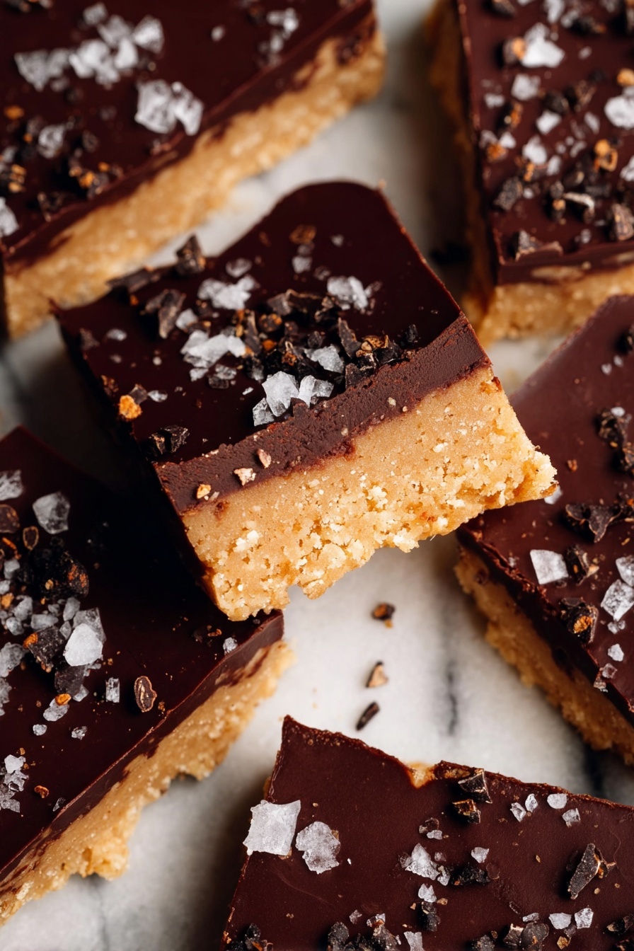 A stack of seven thick, square bars is shown, each with two layers: a bottom layer of light brown, crumbly cookie dough filled with small, dark chocolate chips, and a top layer of smooth, dark chocolate that is solid and shiny. One bar lies flat in front of the stack, displaying the same two layers and sprinkled with a few grains of salt on the dark chocolate surface. The bars are placed on a white speckled plate, which sits on a white marbled surface. The focus is sharp on the bars, capturing the texture of the cookie dough and the gloss of the chocolate, with a soft, blurred background. Photo taken with an iphone --ar 2:3 --v 7 - Healthy Protein Cookie Dough Bark, healthy protein snacks, guilt-free cookie dough treats, quick healthy dessert, high-protein sweet bites