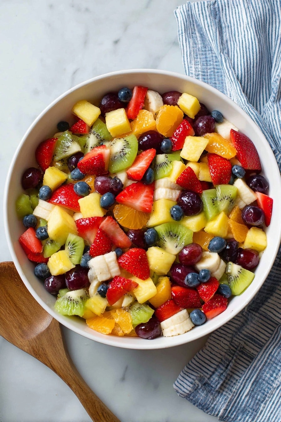 A large white bowl filled with a colorful mix of fruit pieces, layered together. There are bright red strawberry halves, yellow pineapple chunks, green kiwi slices, deep blue blueberries, orange mandarin slices, purple grape halves, and white banana pieces, all mixed evenly. The fruits show a fresh and juicy texture, with the bowl set on a white marbled surface. A striped blue and white cloth is partially visible to the top right, and a wooden spoon is at the bottom left beside the bowl. photo taken with an iphone --ar 2:3 --v 7 - Colorful Honey Lime Rainbow Fruit Salad, rainbow fruit salad, healthy fruit salad, quick fruit salad recipe, summer fruit salad
