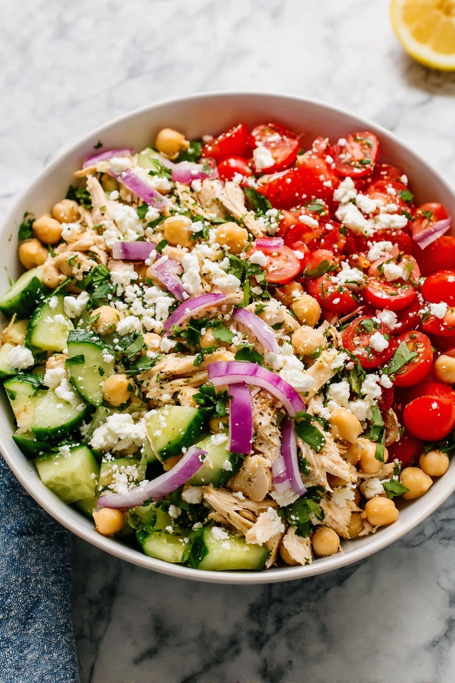 A white bowl filled with a colorful layered salad sits on a white marbled surface. The salad has several layers: at the bottom, light green cucumber slices and bright red cherry tomato halves mixed with beige chickpeas. Scattered above are thin strips of light beige cooked chicken, thin purple-red onion slices, and fresh green herbs. Crumbled white cheese is sprinkled evenly on top, adding texture and contrast. The combination of red, green, purple, beige, and white colors creates a fresh and vibrant look. Photo taken with an iphone --ar 2:3 --v 7 - Healthy Chickpea Tuna Salad with Fresh Veggies, healthy tuna salad, quick nutritious lunch, easy chickpea tuna recipe, fresh veggie salad