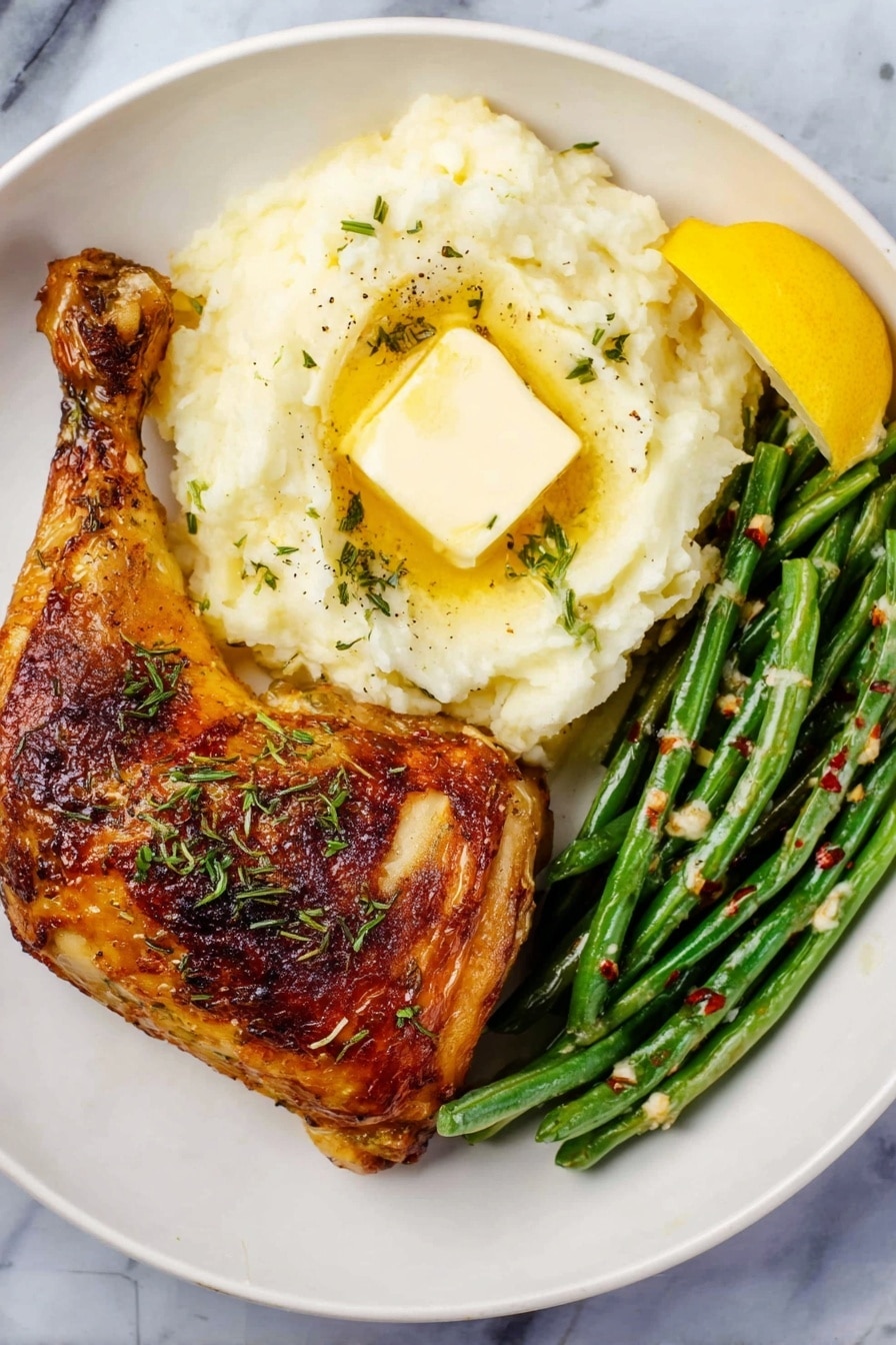 A white round plate holds three main parts of the meal. On the left side is a large roasted chicken leg with golden brown, crispy skin and some green herbs sprinkled on top. On the right side, there is a creamy mound of mashed potatoes with a square pat of melting butter in the center and small bits of green herbs scattered over it. Below the mashed potatoes, there is a neat row of cooked green beans with a slight shine and some red pepper flakes for color. A wedge of bright yellow lemon is placed at the top right edge of the plate. The plate sits on a white marbled surface. Photo taken with an iphone --ar 2:3 --v 7 - Crispy Baked Chicken Legs with Herbs, Juicy baked chicken thighs, Easy baked chicken recipes, Herbed chicken dinner, Healthy baked chicken ideas