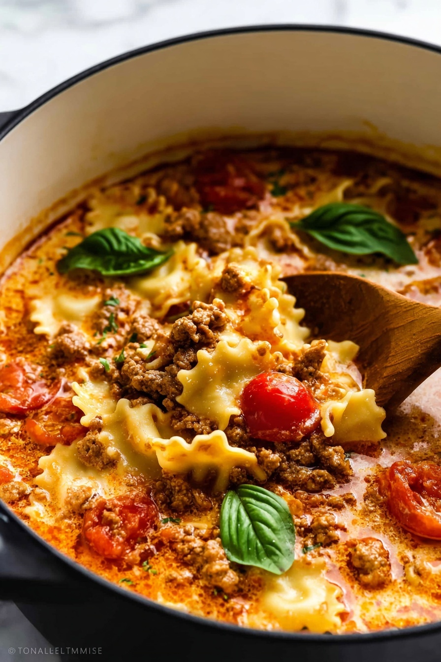 This image shows a close-up of a pot filled with a creamy lasagna soup. The dish has three main layers: the bottom layer is a rich tomato broth with creamy swirls, the middle layer has crumbled cooked ground meat with a brown color and a slightly crumbly texture, and the top layer includes wavy lasagna pasta pieces in a pale yellow color that float on the surface. There are whole cherry tomato pieces adding splashes of bright red throughout the soup. On top of the pasta and meat mixture sit a few fresh, green basil leaves, giving a fresh contrast to the warm colors. A wooden spoon dips into the soup from the side, stirring the ingredients gently. The pot is white with a black interior, sitting on a white marbled surface. photo taken with an iphone --ar 2:3 --v 7 - Lasagna Soup with Ricotta Basil Topping, easy Italian lasagna soup, cheesy lasagna soup recipe, quick lasagna-inspired soup, flavorful ricotta basil topping