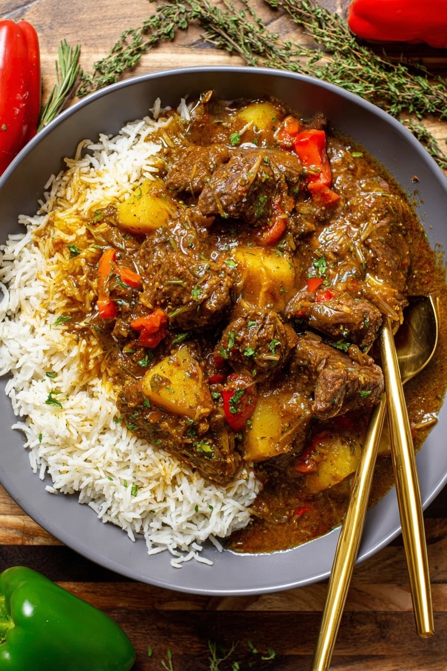 The image shows a deep bowl filled with a base layer of white rice spread evenly. On top of the rice, there is a rich, thick stew with dark brown pieces of meat, chunks of yellow potatoes, and visible red bell pepper slices. The stew looks moist and glossy, covering the rice partly, with the sauce seeping into the rice edges. Two gold spoons rest inside the bowl on opposite sides. The bowl sits on a wooden surface with a green pepper, a red pepper, and some sprigs of green herbs scattered nearby. Photo taken with an iphone --ar 2:3 --v 7 - Jamaican Curry Chicken, Jamaican Curry Chicken recipe, Caribbean chicken curry, spicy Jamaican chicken, Jamaican chicken dinner