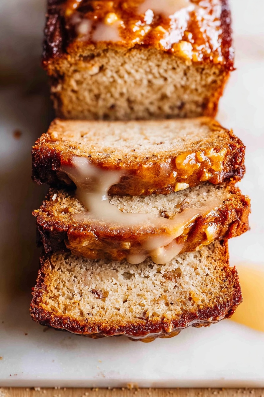 The image shows a close-up of a sliced loaf of moist cake with three visible slices neatly stacked on a white marbled surface. The cake has a golden brown crust with a slightly darker, caramelized edge. The inside is light brown and textured with small pieces of fruit or nuts evenly spread throughout. There is a glossy, light-colored syrup or glaze dripping around the top slice, pooling slightly on the surface. The top of the loaf looks dense and shiny due to the syrup. photo taken with an iphone --ar 2:3 --v 7 - Amish Apple Fritter Bread, apple fritter bread with glaze, cinnamon apple bread, easy apple bread recipe, sweet apple bread dessert